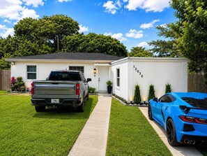 Ein Wohnhaus mit Auffahrt, ein weißes Haus, ein blauer Sportwagen und ein Pritschenwagen.
