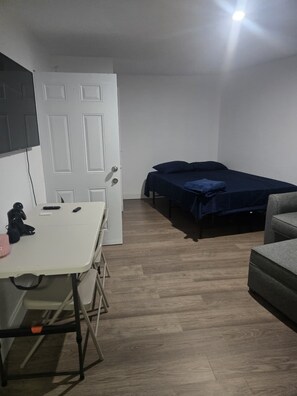 A room with a bed, a desk, and a chair. There is a door with a handle, and a light fixture on the ceiling. - Beautiful 1-bedroom house with AC in fantastic North Miami (North Miami)