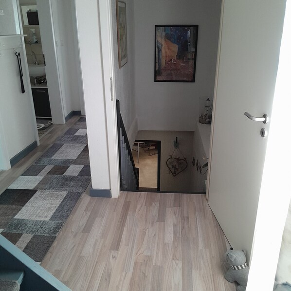A hallway with a patterned carpet, a painting on the wall, and a teddy bear on the floor.