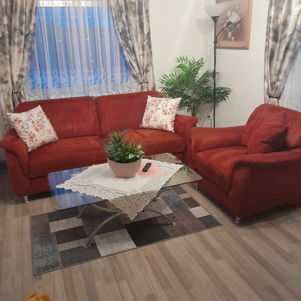 Ein Wohnzimmer mit einem roten Sofa, einem kleinen Tisch mit einer Pflanze und einer Stehlampe.
