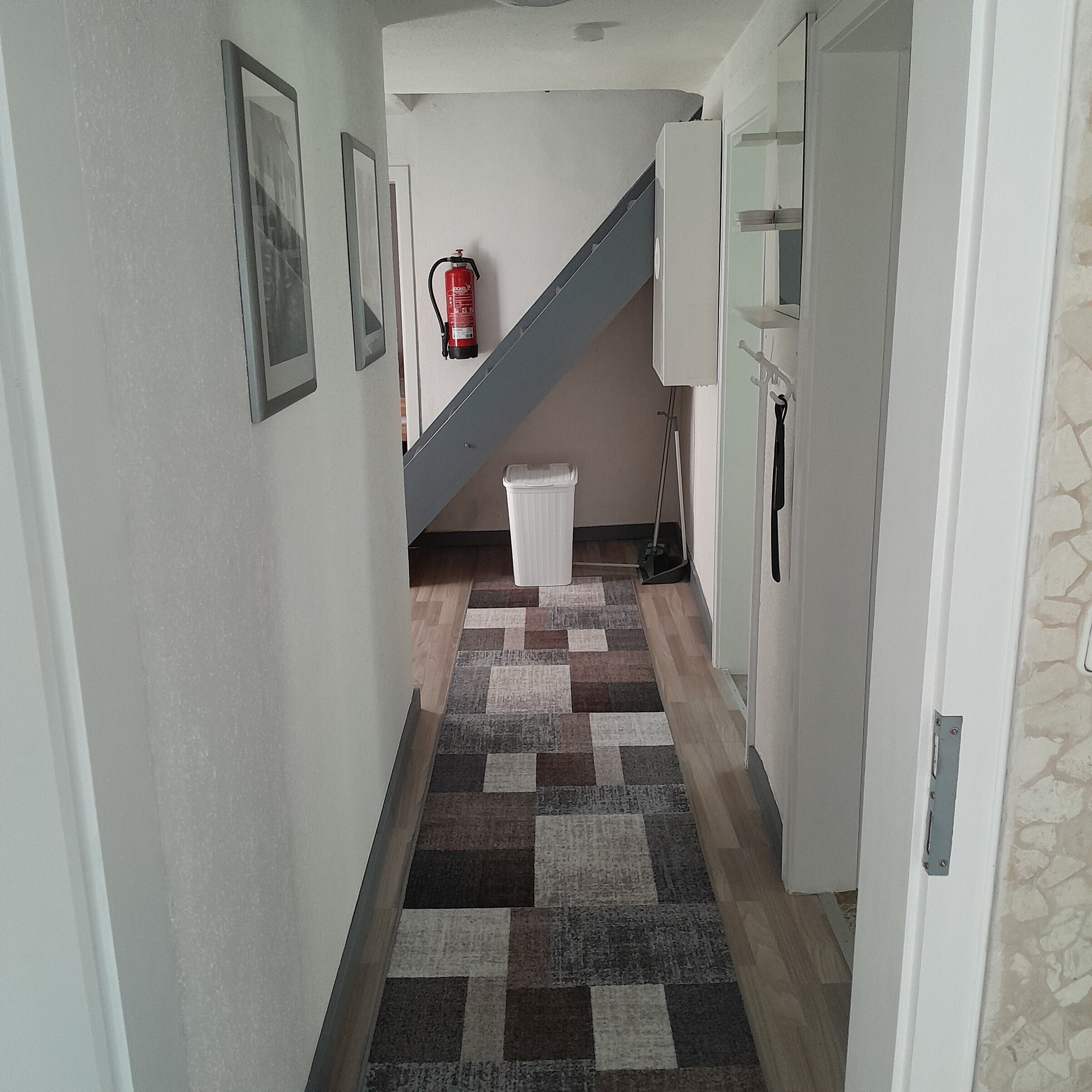 Ein Korridor mit einem gemusterten Teppich, einem an der Wand befestigten Feuerlöscher und einer Treppe, die zu einer anderen Etage führt.