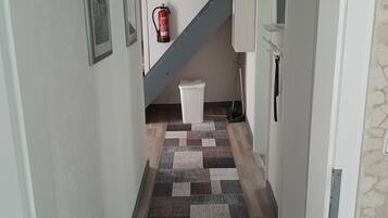 Ein Korridor mit einem gemusterten Teppich, einem an der Wand befestigten Feuerlöscher und einer Treppe, die zu einer anderen Etage führt.