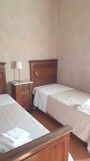 A bedroom with two beds, wooden headboards, a nightstand with a lamp, and a small cabinet. - A charming historic farmhouse, 10 minutes from Orvieto, with a garden and private pool, (Umbria)