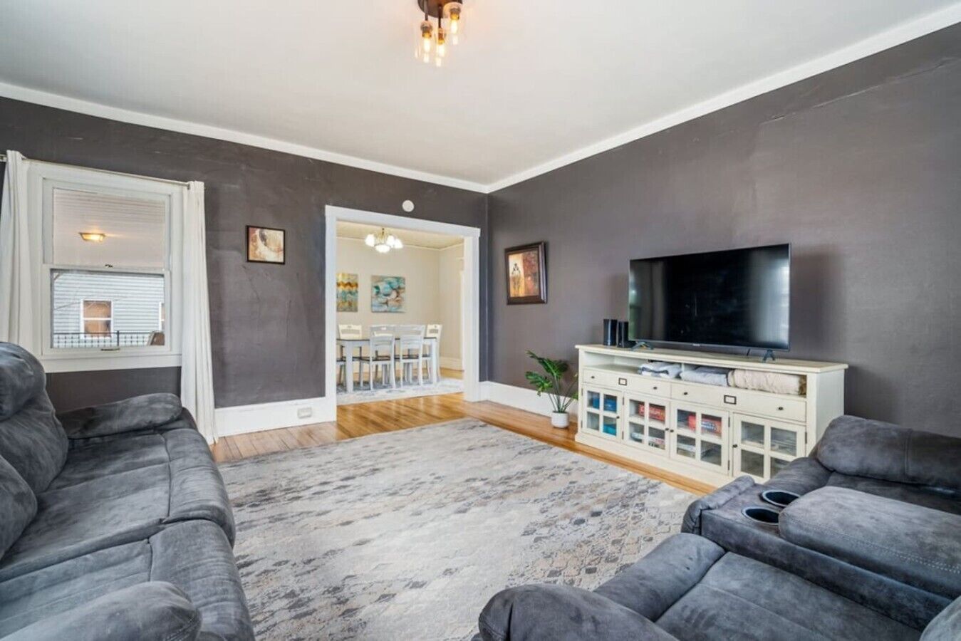 Un salon avec un canapé gris, un t éléviseur à écran plat et un meuble avec des portes en verre.