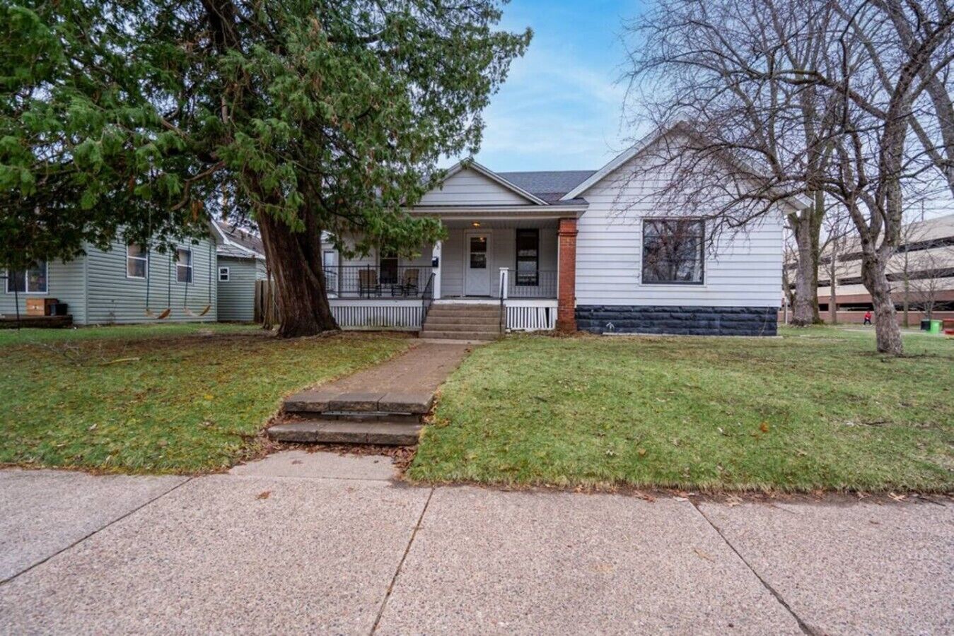 A two-story house with a front porch, a small front yard, and a driveway leading to the entrance.