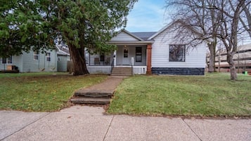 A two-story house with a front porch, a small front yard, and a driveway leading to the entrance.