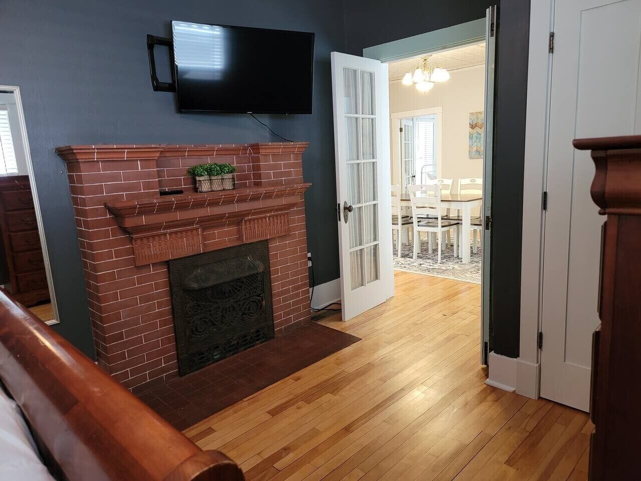 A living room with a brick fireplace, a flat-screen TV mounted above it, and a wooden floor.