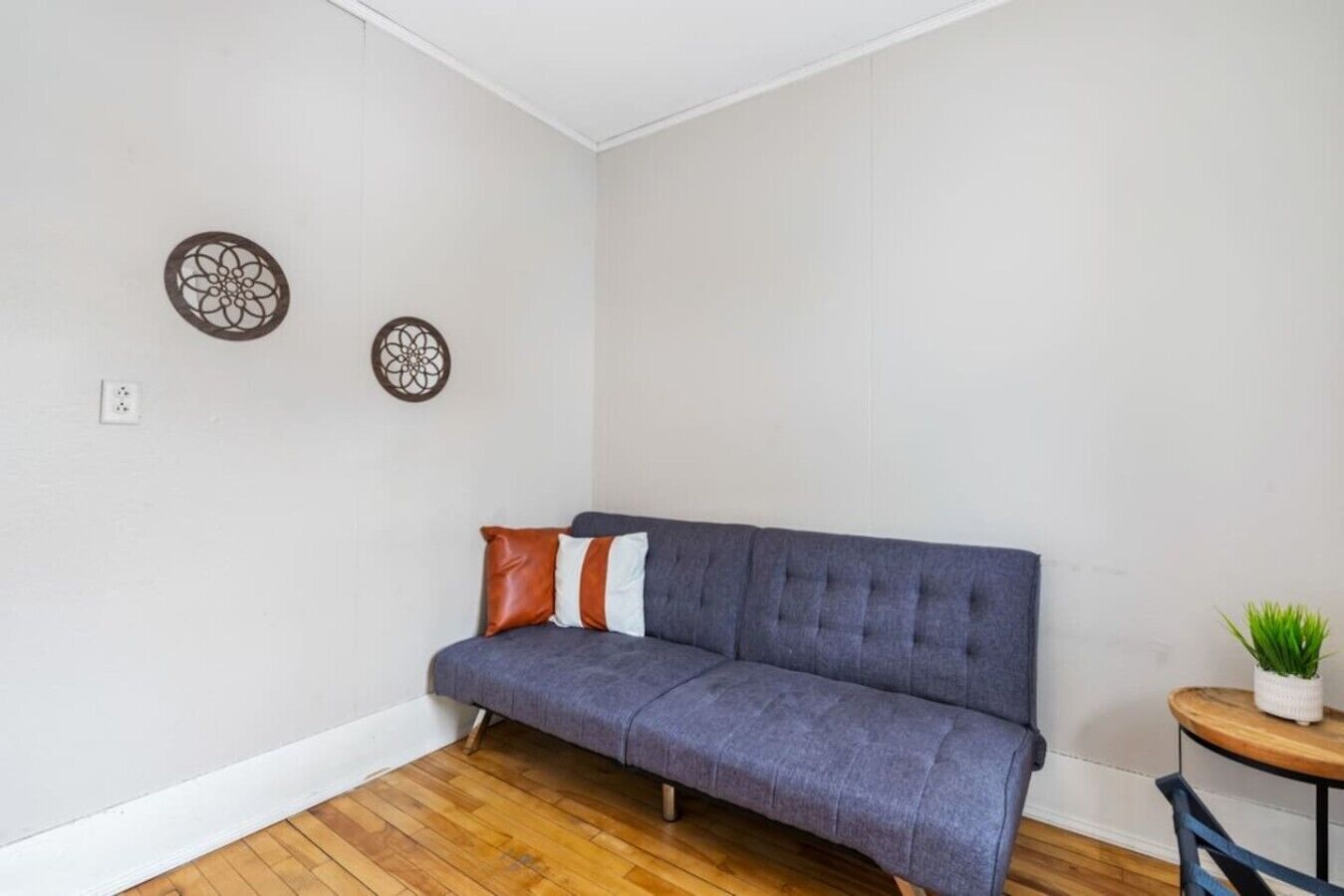 A room with a grey sofa, a small round table with a plant, and two wall decorations.