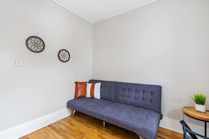 Una habitació amb un sofà gris, una taula rodona petita amb una planta i dues decoracions murals.