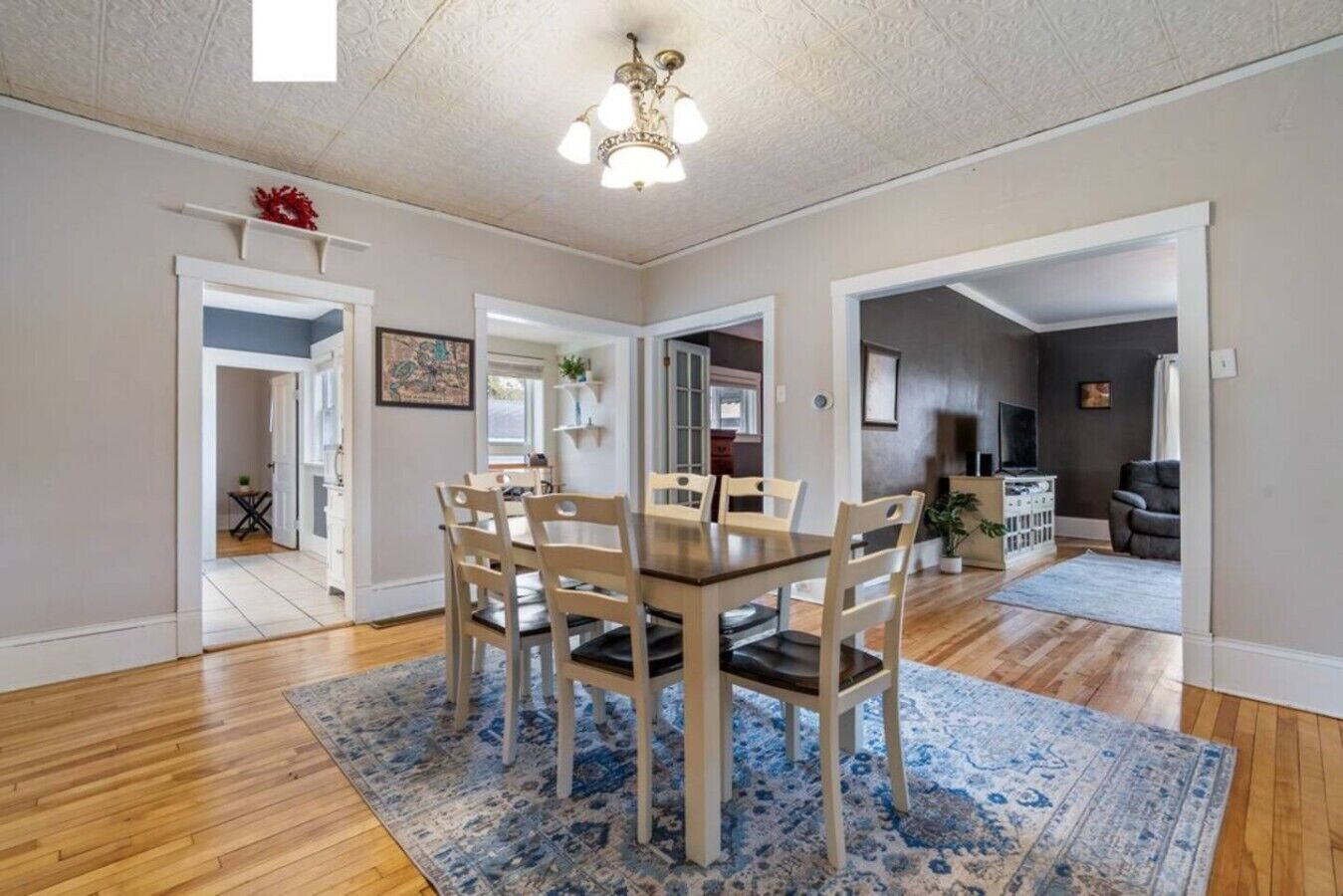 A dining area with a wooden table and chairs, a blue patterned rug, and a ceiling light fixture.