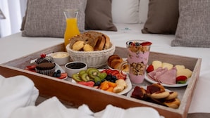 A breakfast tray with various foods and a glass of orange juice on a bed.