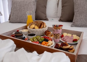 A breakfast tray with various foods and a glass of orange juice on a bed. - ONLY Design Suites & Spa (Mar de Las Pampas)