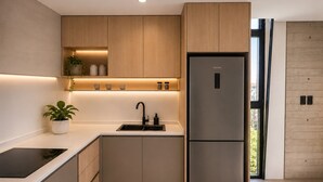 A modern kitchen with wooden cabinets, a stainless steel refrigerator, a sink, and a potted plant.