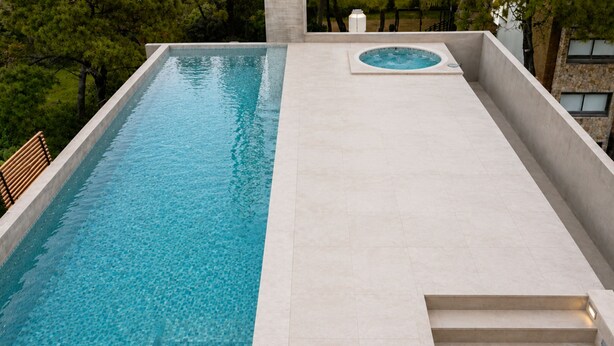 A rectangular swimming pool with a clear blue water surface, surrounded by a light-colored tiled deck.