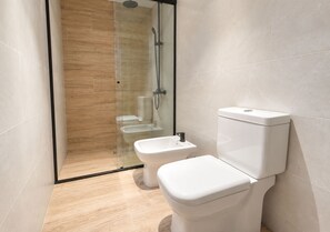 A modern bathroom with a glass-enclosed shower, a toilet, and a bidet.