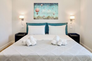 Een hotelkamer met een bed, twee bedlampen, een schilderij van luchtballonnen en twee opgerolde handdoeken op het bed.