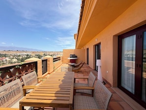 Un balcone con tavolo e sedie in legno, un barbecue e vista sulla città.