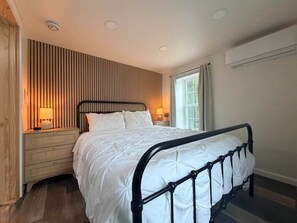 A bedroom with a bed, bedside tables, a window, and a wall-mounted air conditioner. - Sheldrake Point Suite, Ovid (Ovid)