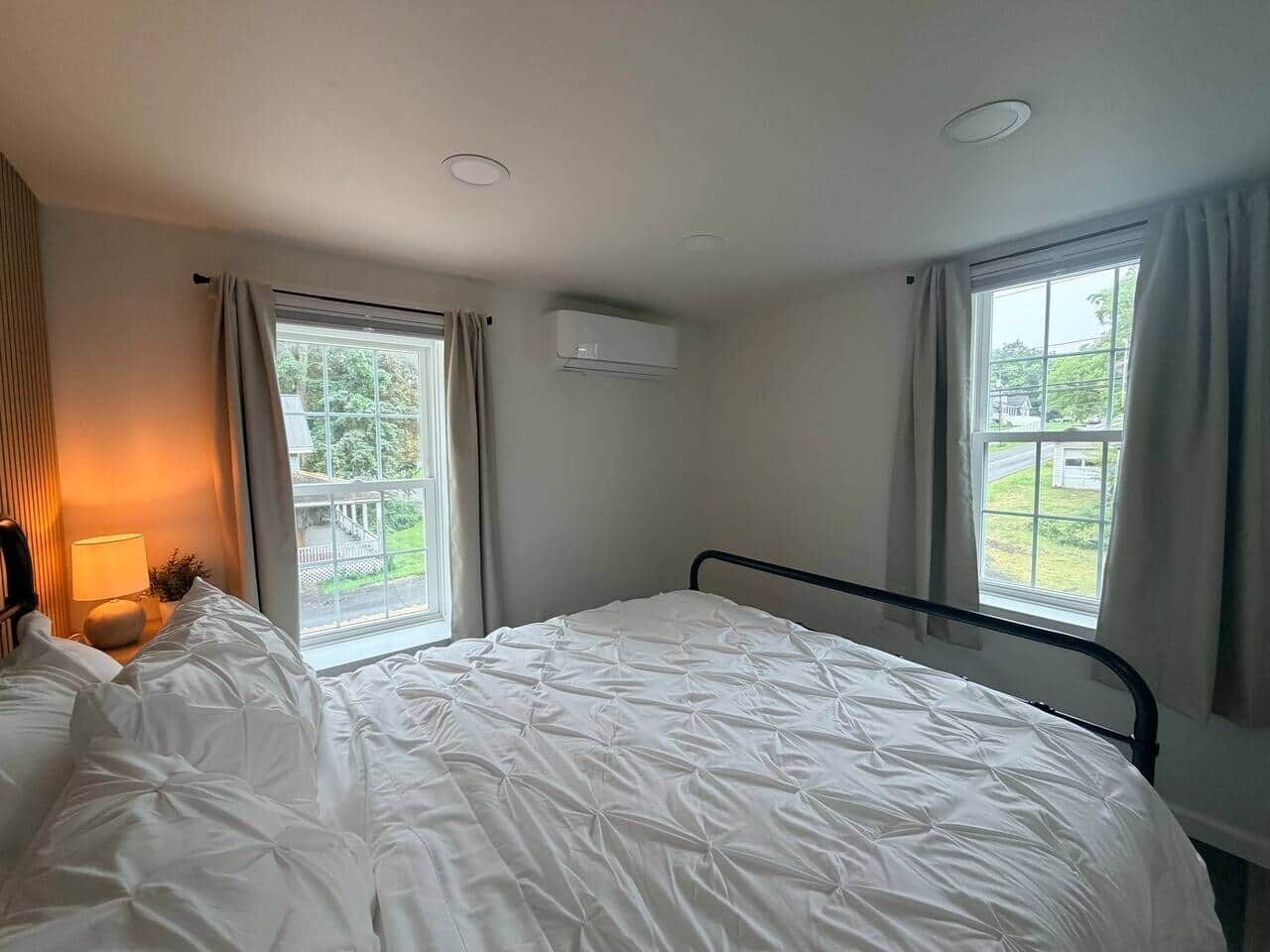 A hotel room with a single bed, a bedside table with a lamp, and two windows with curtains.
