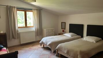 Een slaapkamer met twee bedden, een radiator, een raam met gordijnen, een nachtkastje met een lamp en een spiegel aan de muur.