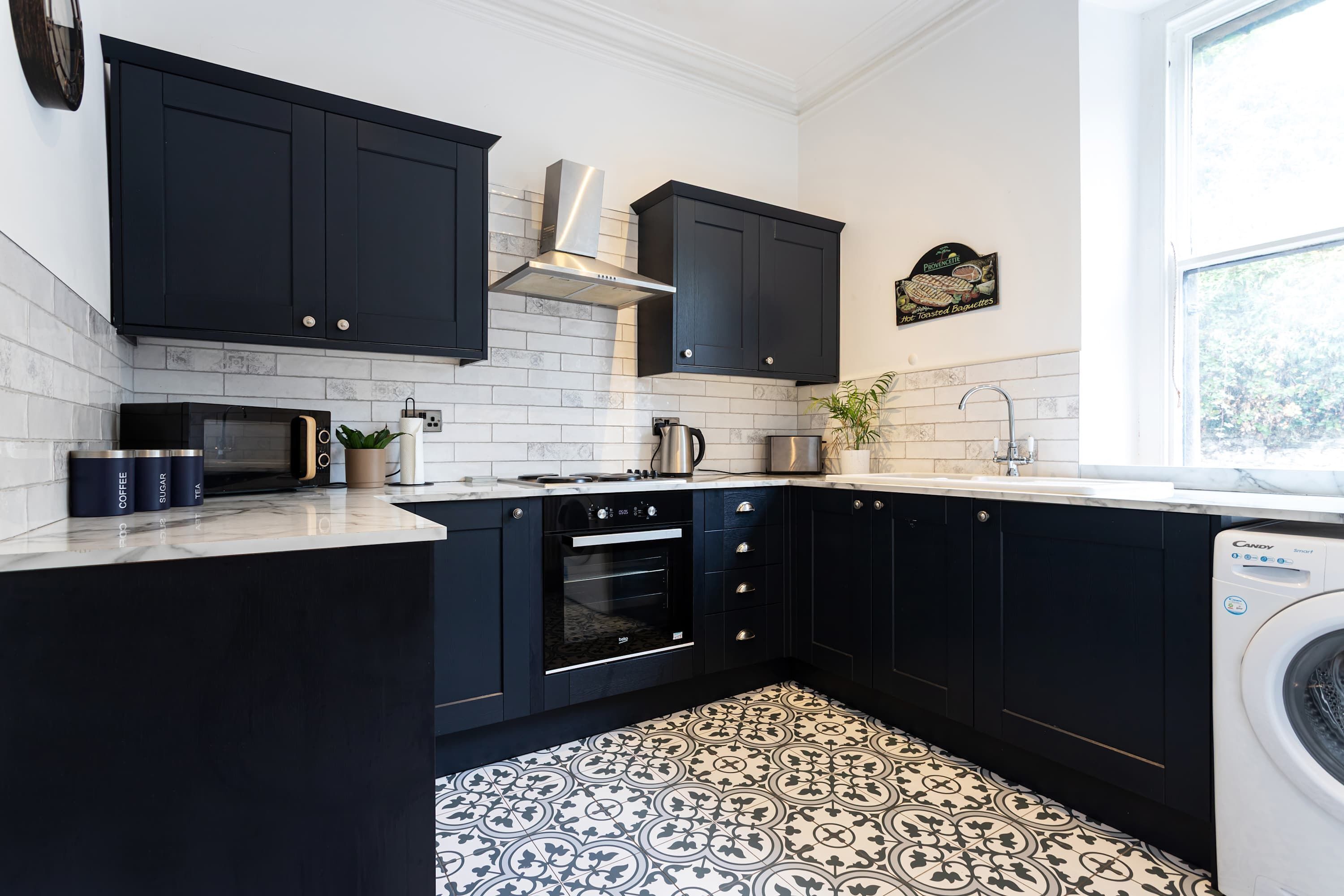 Una cocina moderna con armarios negros, horno empotrado, microondas y lavadora.