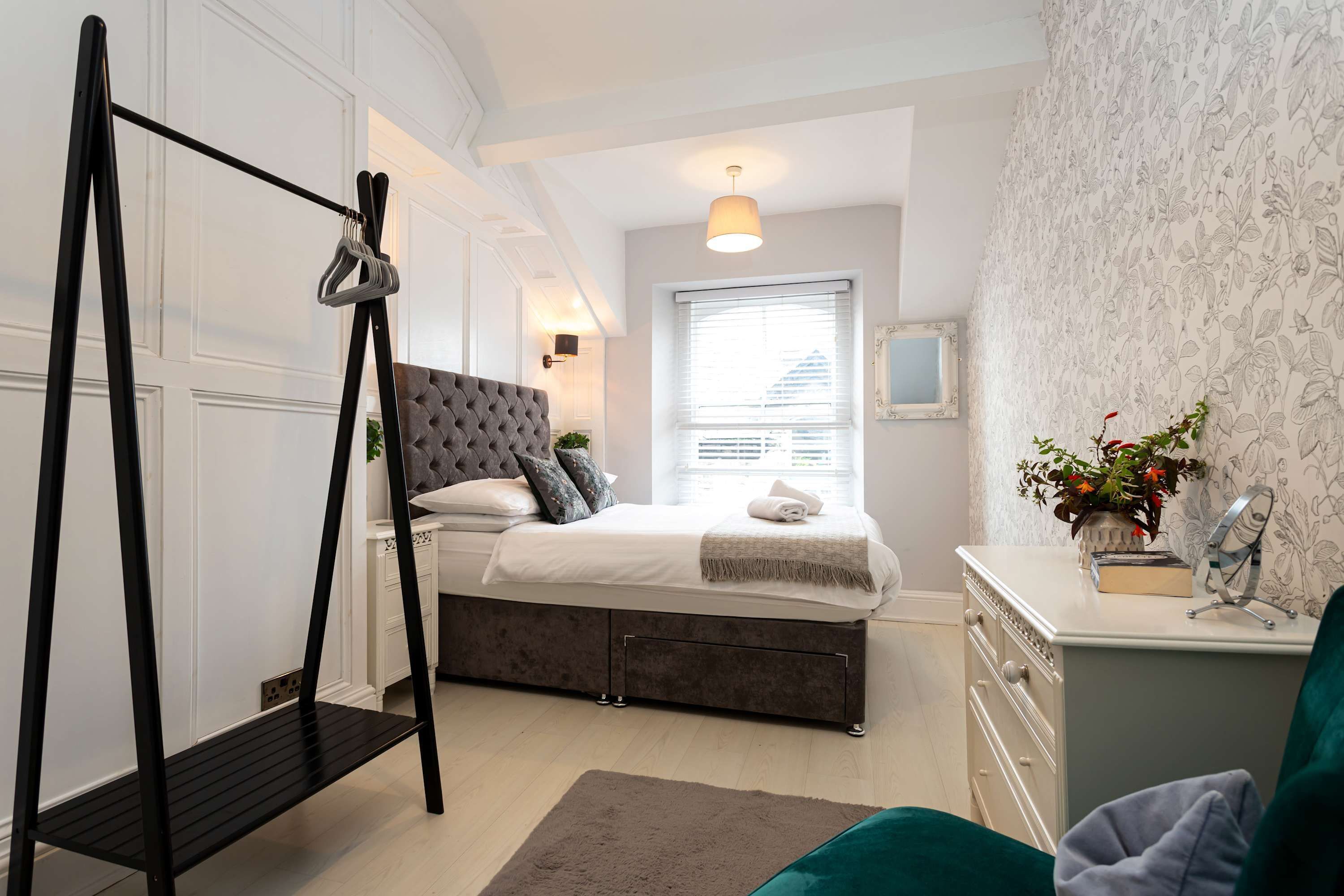 Une chambre à coucher comprenant un lit, une table de chevet, une commode et une étagère en métal noir.