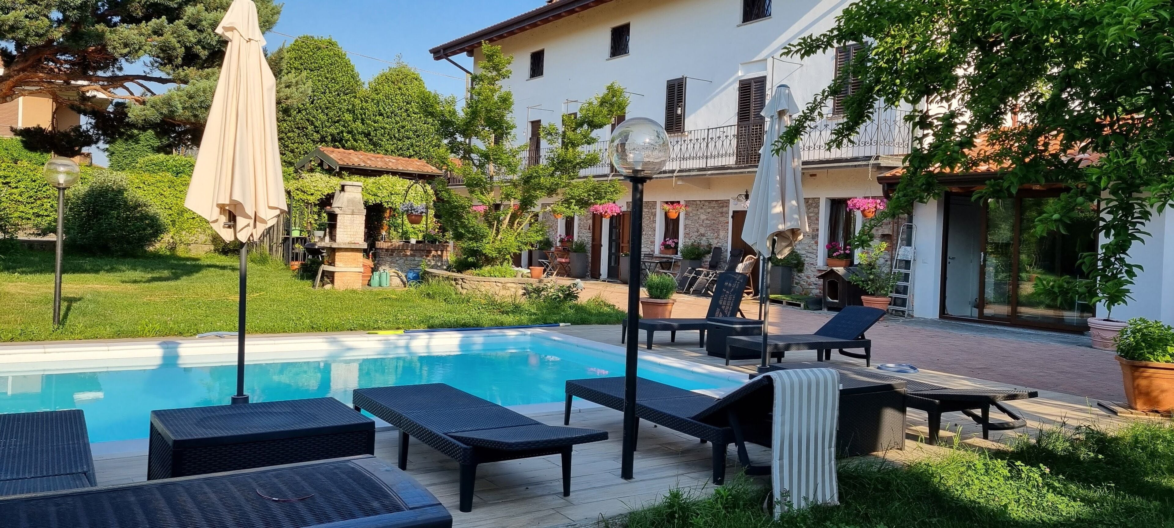 A pool area with lounge chairs and umbrellas, surrounded by greenery and a building with stone walls.