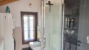 Et moderne badeværelse med et glasafskærmet brusebad, toilet og vaskemaskine.
