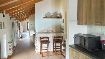 Een keuken met houten kastjes, een magnetron en een eethoek met stoelen.