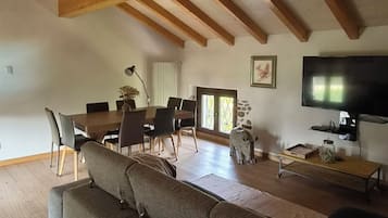 Ein geräumiges Wohnzimmer mit hohen Decken, Holzbalken, einem großen Sofa, einem Esstisch, Stühlen, einem Fernseher und einer Steinskulptur.