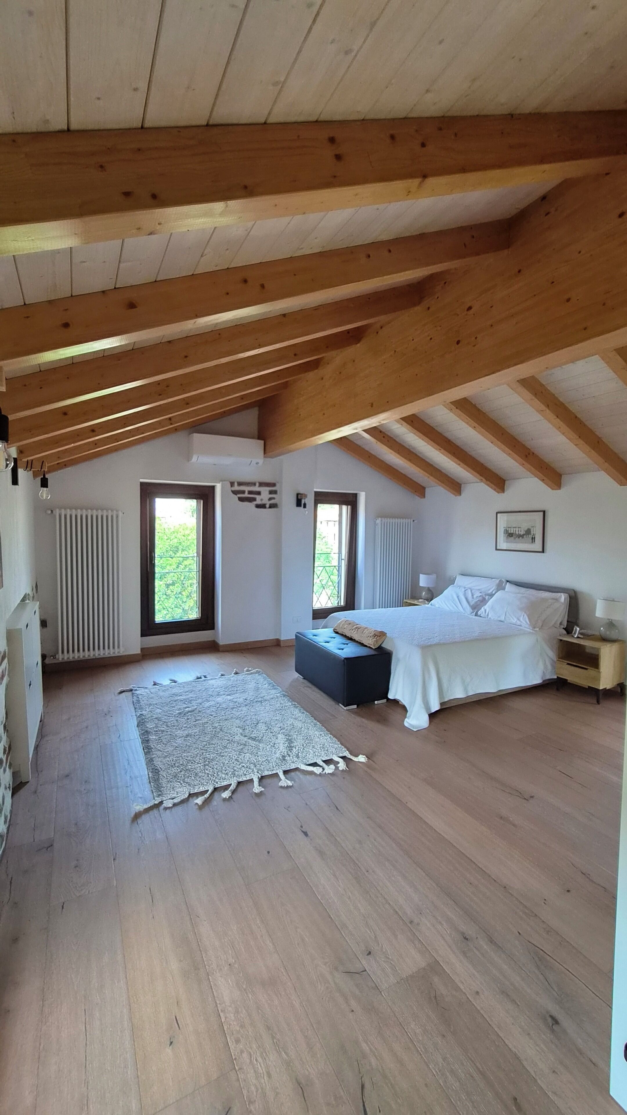 Ein Schlafzimmer mit einem großen Bett, einem Nachttisch, einem Fenster und Blick auf Grün.