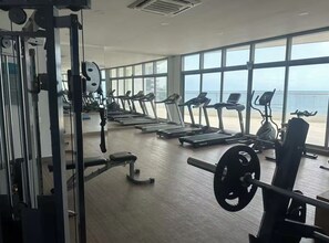 A gym with cardio machines, weightlifting equipment, and large windows overlooking the sea. - APARTMENT WITH A SEA VIEW (Cartagena de Indias)