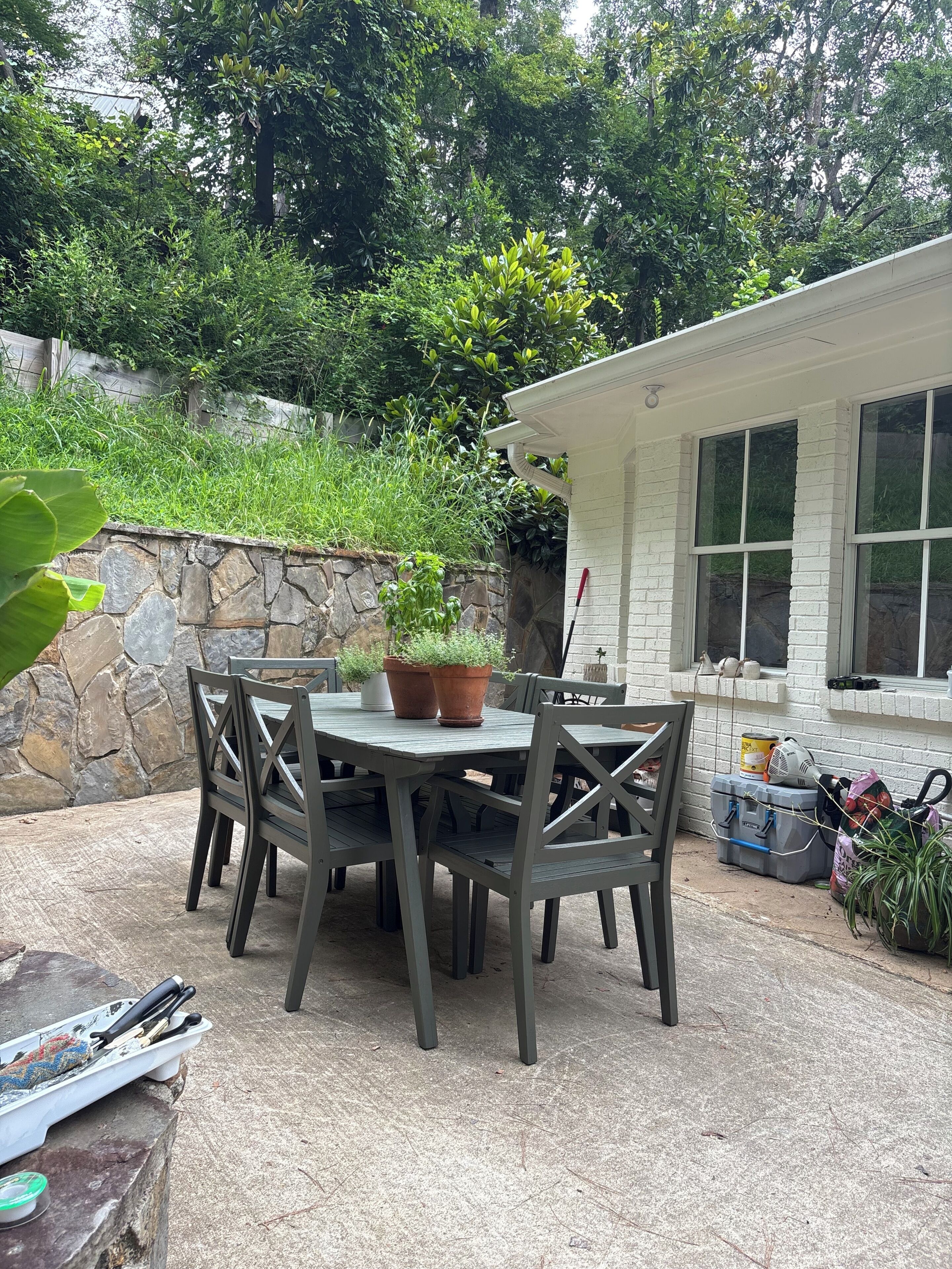 Un patio al aire libre con una mesa y sillas, rodeado de un muro de piedra y follaje.