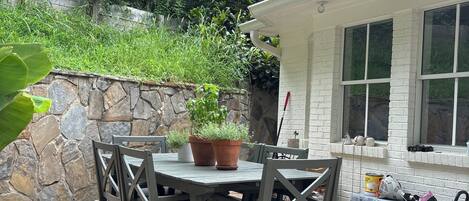 Un patio al aire libre con una mesa y sillas, rodeado de un muro de piedra y follaje.