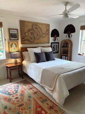 A bedroom with a large bed, a wooden nightstand, a map on the wall, a bookshelf, and a decorative fan.