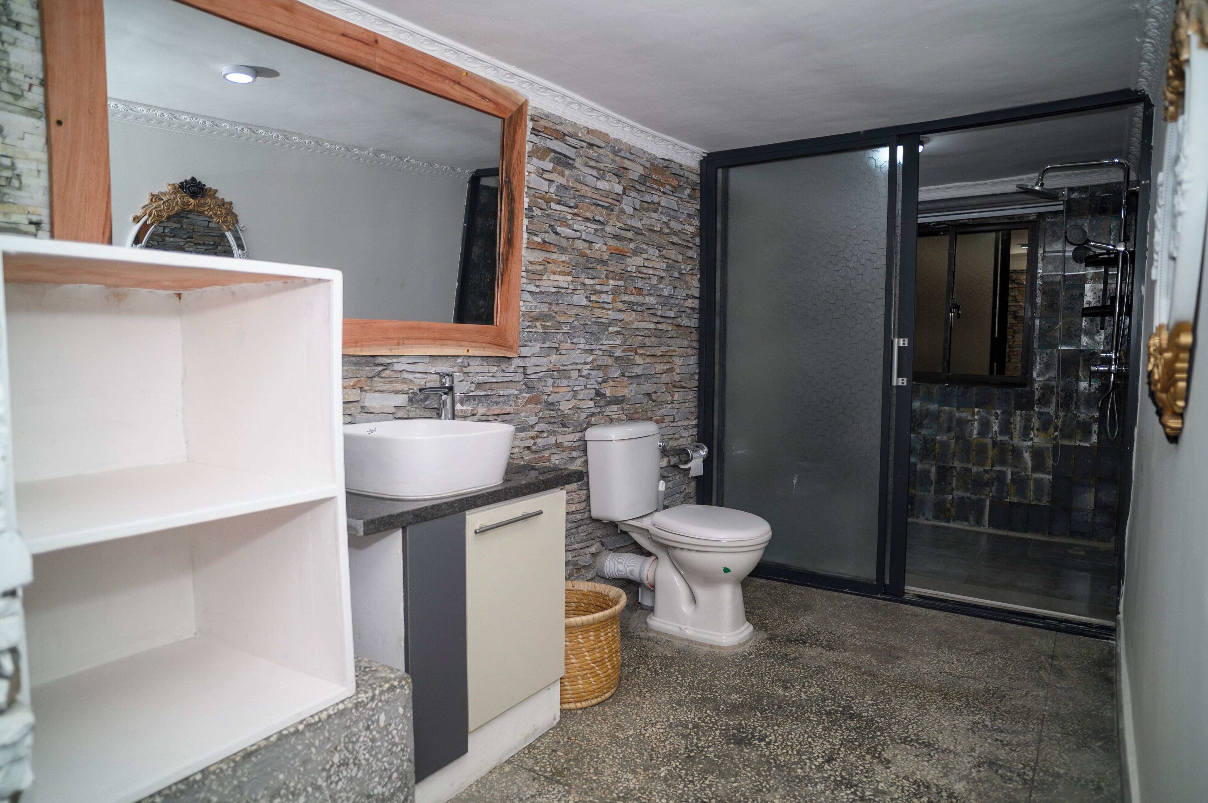 A bathroom with a stone wall, a white sink, a toilet, and a shower area.