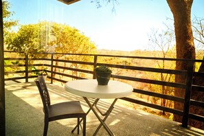 A balcony with a round table and a chair, a potted plant, and a view of trees and hills. - Sunset Villa at Forest Hill House (LUSAKA)