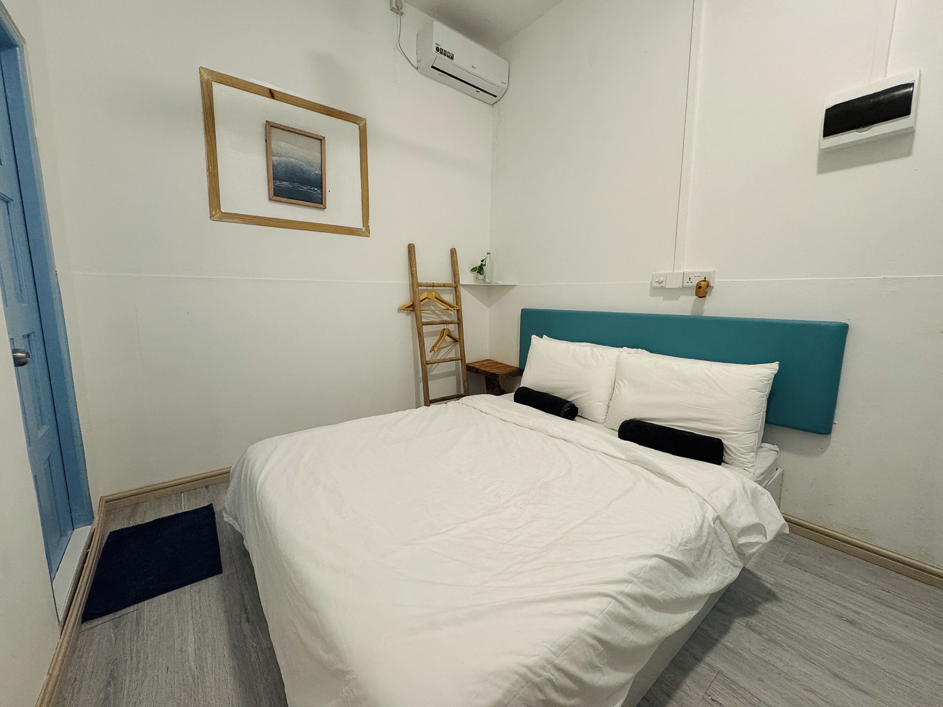 Une chambre d’hôtel avec un lit, un climatiseur fixé au mur, un tableau encadré et une échelle en bois.