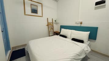 A hotel room with a bed, a wall-mounted air conditioner, a framed picture, and a wooden ladder.