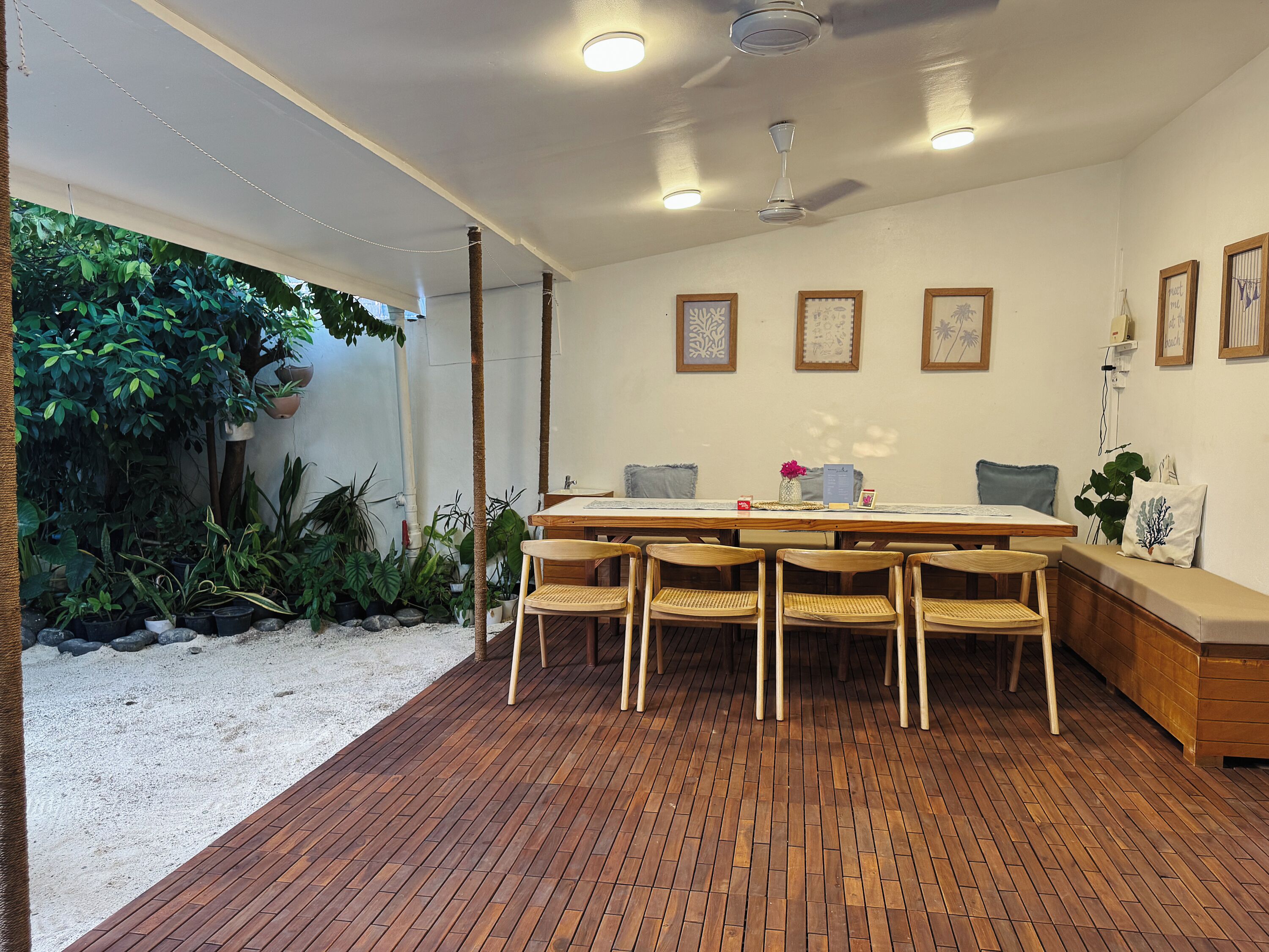 A dining area with a wooden table and chairs, surrounded by potted plants and a view of greenery.