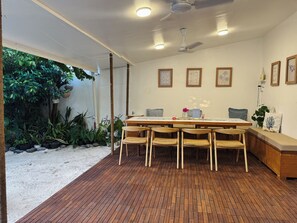 A dining area with a wooden table and chairs, surrounded by potted plants and a view of greenery.