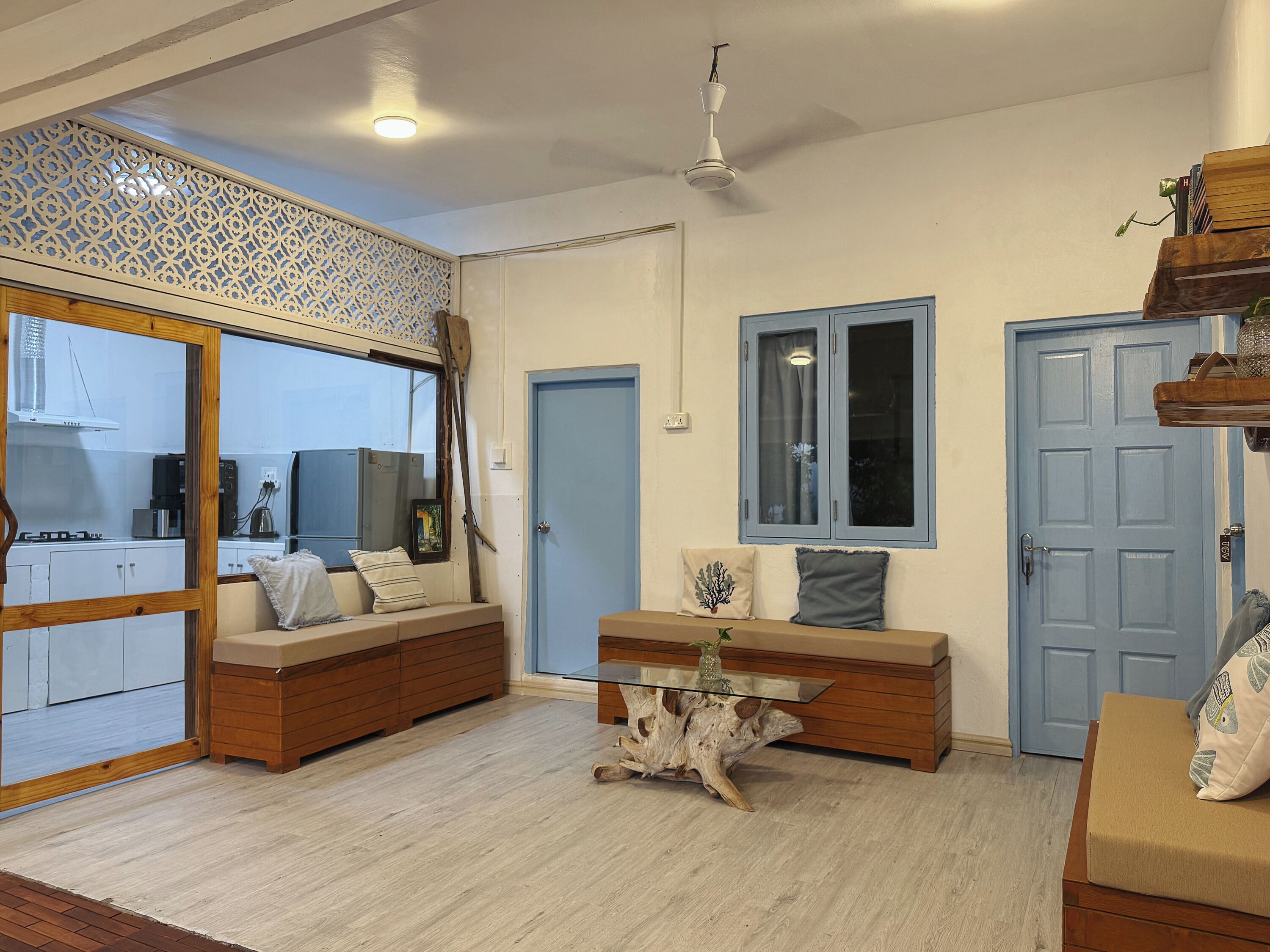 A room with a wooden bench, a glass coffee table, and a blue door.