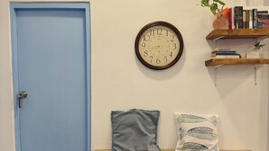 Una habitación con una puerta azul, un reloj de pared, una estantería y un banco con almohadones.