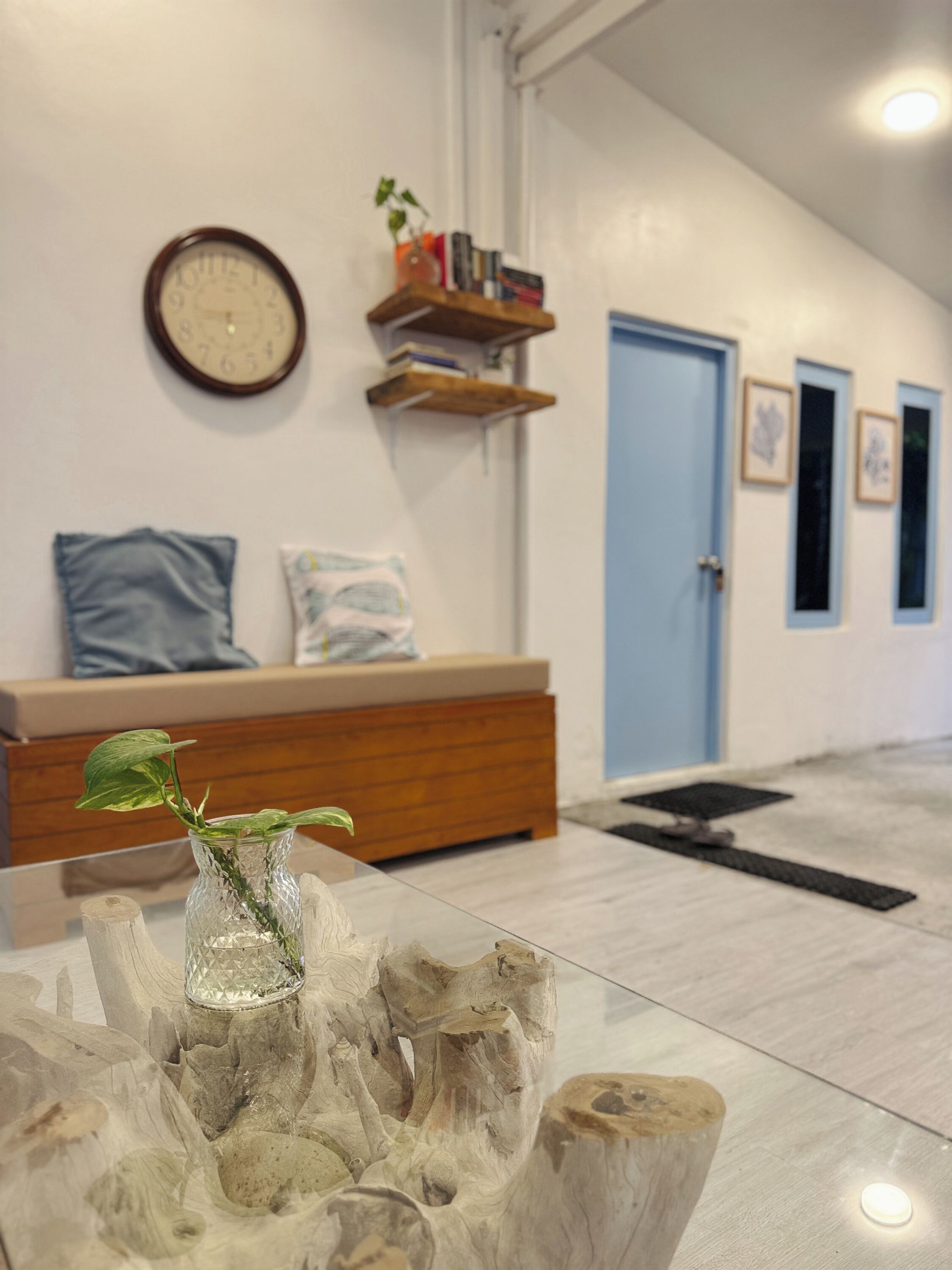 A modern interior with a wooden reception desk, a wall clock, and a glass vase with a plant on a glass table.