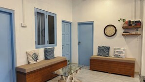 Una habitación con dos puertas azules, una mesa de centro de vidrio con base de madera, un reloj en la pared y una estantería con libros y una planta pequeña.