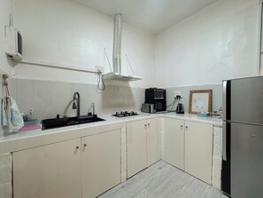 A kitchen with a gas stove, a microwave, a kettle, and a refrigerator.