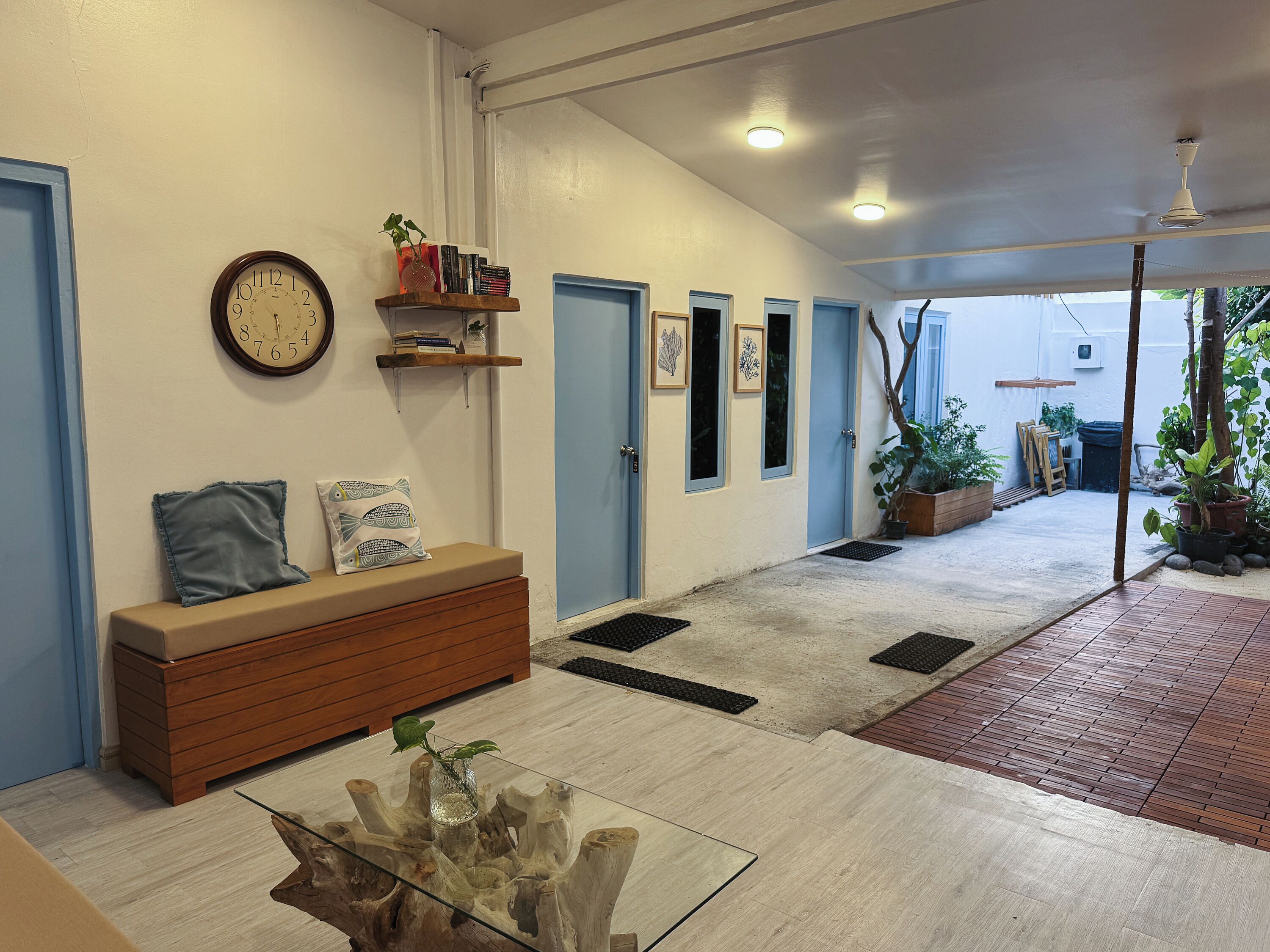 A hallway with a wooden bench, a glass coffee table, a clock, and a door with a blue frame.