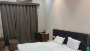 Una habitación de hotel con cama, mesita de noche, silla y aire acondicionado.