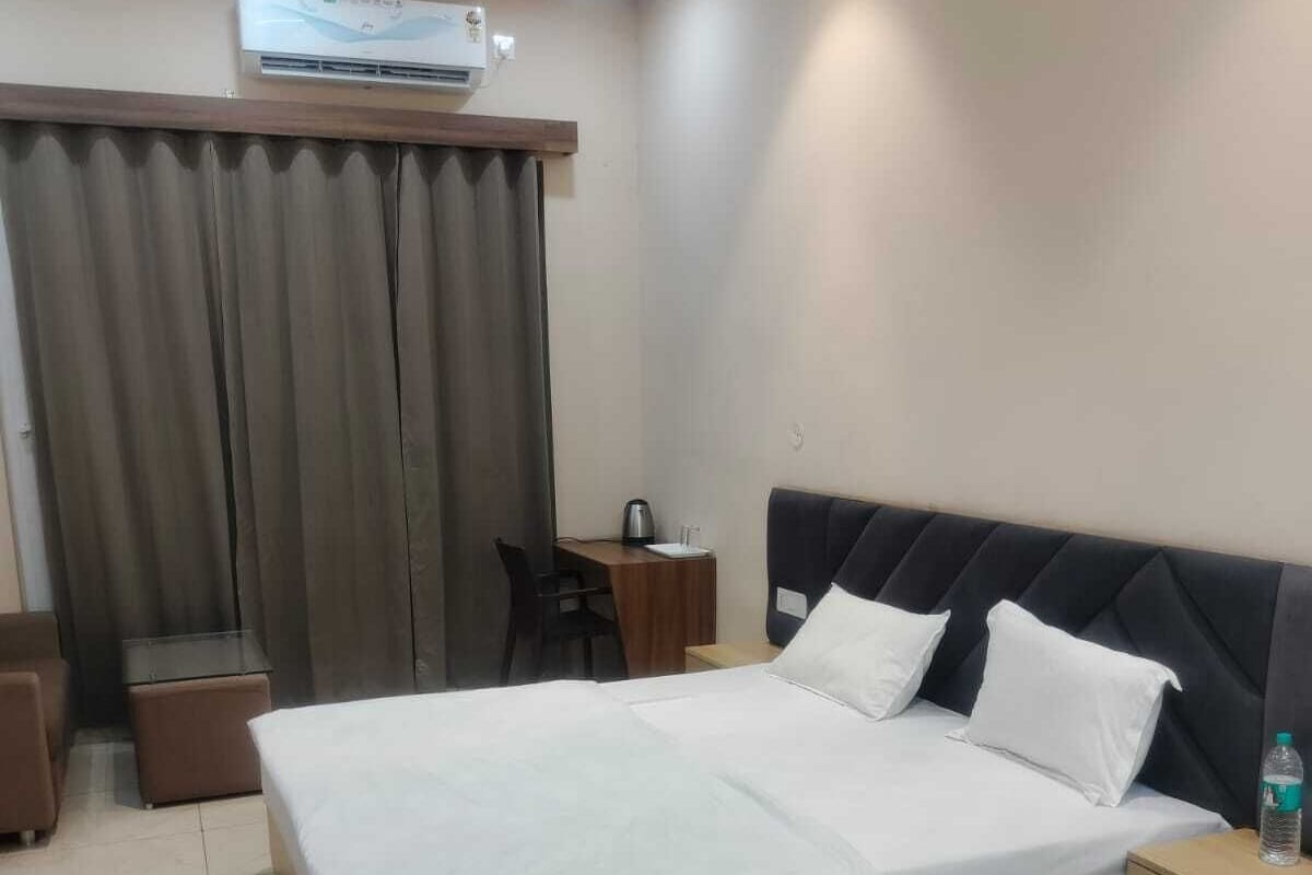 A hotel room with a bed, bedside table, chair, and an air conditioning unit.