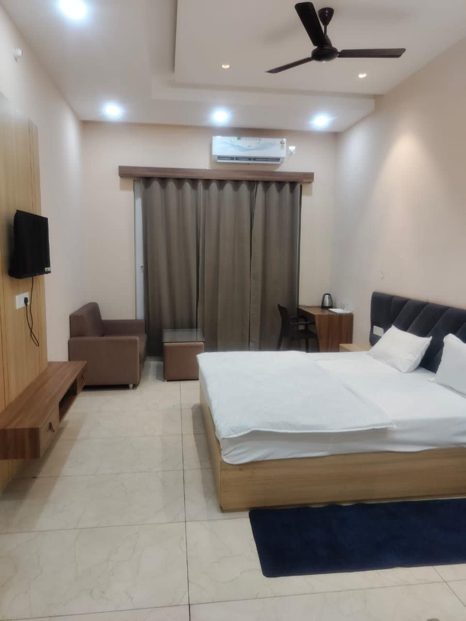 Habitación de hotel con cama, escritorio, silla, televisor y ventilador de techo.